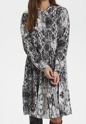 Sukienka w czarno-biały wzór z kołnierzykiem, długimi rękawami i plisowaną częścią spódnicy, wykonana z lekkiego materiału.