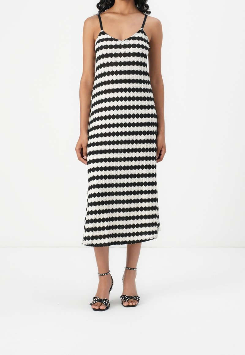 Femme portant une robe midi sans manches rayée noir et blanc avec des talons à brides cheville noirs ornés de nœuds et de clous.