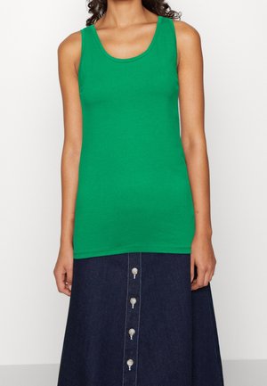 Woman wearing a sleeveless green tank top paired with a dark blue buttoned denim skirt standing against a plain white background.