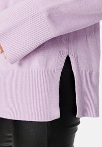 Maglione lilla lavorato a maglia con polsini e orlo a coste, caratterizzato da fessure laterali. Indossato sopra Leggings neri, evidenziando il contrasto di texture e colore.