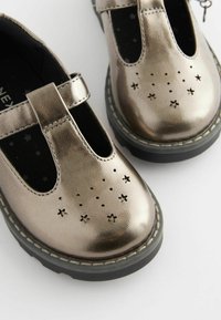 Metallisch bronzefarbene Leder-Schuhe im Mary-Jane-Design, mit sternförmigen Ausschnitten und einer schwarzen Gummisohle. Mit einem einzigen Riemen über dem oberen Teil.