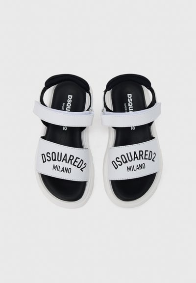 Άσπρες σανδάλες slide με μαύρη σόλα, με φαρδιά λουρίδα που φέρει την επιγραφή "DSQUARED2 MILANO" σε μαύρο χρώμα. Λείο υλικό, καθημερινό σχέδιο.
