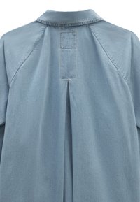 Vaaleansininen paita, jossa on kaulus, takakeskittymä ja raglansovitukset, valmistettu pehmeästä, teksturoidusta kankaasta.