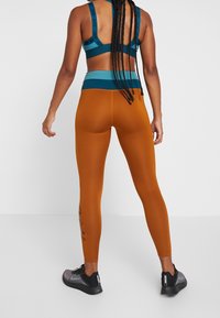 Set di reggiseno sportivo e leggings in teal e arancione. I leggings presentano un motivo testurizzato con logo lungo il lato. Il materiale appare elastico e liscio.