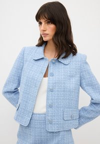 Giacca in tweed a trama blu chiaro con colletto, sei bottoni metallici e taschino applicato. Design con maniche lunghe e silouette aderente.