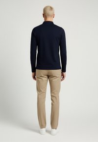 Polo a maniche lunghe blu navy con colletto, abbinato a pantaloni beige chiaro su misura e sneakers bianche. Tessuto liscio e design aderente.
