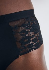 Černé vysoké kalhotky s krajkovým panelem s květinovým vzorem. Hladká látka s kontrastní texturou po stranách, bezšvový design.