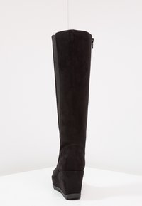 Musta mokka korkkosaapas, jossa on pitkä varsi, sileä pinta, takakuvioinen vetoketju ja muotoiltu pohja tukemiseen.