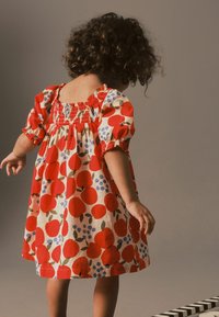 Rød og blå frugtprint kjole med puffærmer, smocket skørt og en samlet nederdel. Stoffet er letvægtsbomuld med en blød tekstur.