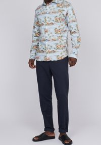 Jasnoniebieska koszula z długim rękawem w tropikalny wzór, z motywem samochodów i palm. Połączona z ciemnoniebieskimi spodniami i czarnymi klapkami.