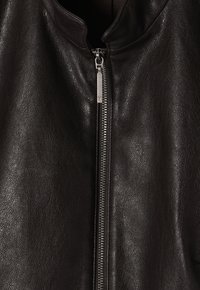 Veste en cuir noir avec un col montant et une fermeture éclair à l'avant. La texture est lisse avec un léger motif de grain.