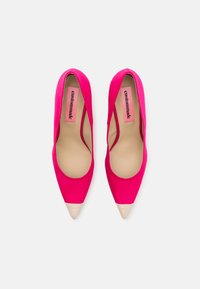 Hot pink high heels with a pointed toe and beige cap toe detail. Smooth fabric exterior with a nude insole and branding visible.