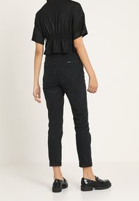 Sort cropped top med en samlet talje, parret med højtaljede, lige ben sorte jeans og glossy sorte sko, set bagfra.