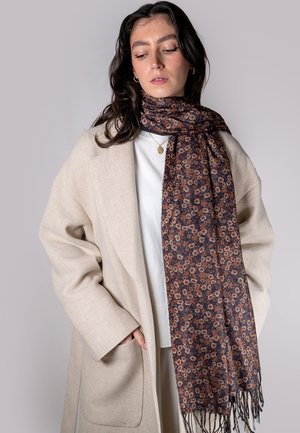 Floral-patterned scarf in dark blue with orange and brown flowers; fringed edges; soft texture; worn with a cream-colored coat.