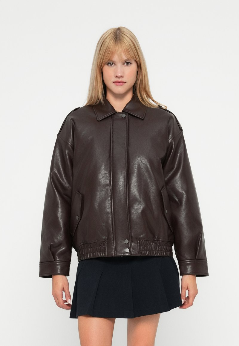 Veste en simili cuir marron avec un col, fermeture à boutons-pression, poches latérales et taille élastique. Coupe oversize avec une finition brillante.