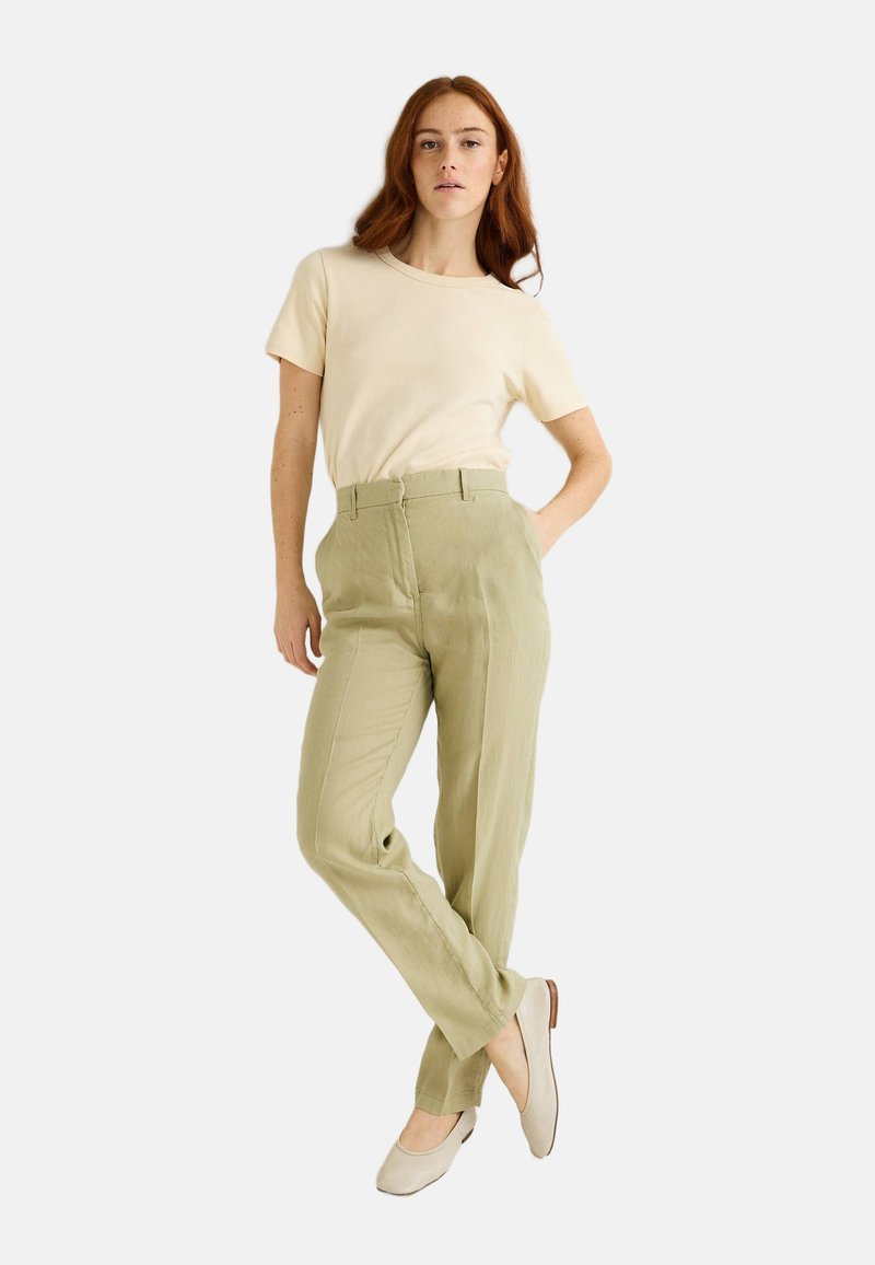 T-shirt beige à manches courtes associé à un pantalon léger vert, bien ajusté. Des ballerines beiges complètent la tenue, avec une texture de tissu lisse.