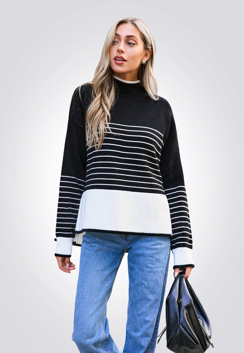 Schwarz-weißer gestreifter Pullover mit hohem Kragen und Rippstruktur, kombiniert mit einer hellblauen Jeans und einer schwarzen Tasche.