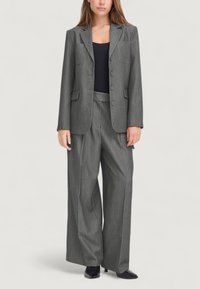 Blazer grigio su misura con pantaloni a gamba larga abbinati, dotato di due tasche frontali e tre bottoni, realizzato in tessuto testurizzato. Top nero sotto.
