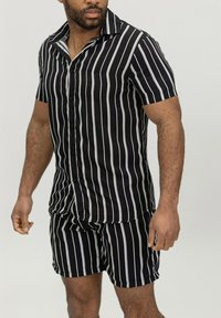 Chemise à manches courtes à rayures noires et blanches avec un short assorti, fabriquée en tissu lisse, présentant des rayures verticales et un col classique.