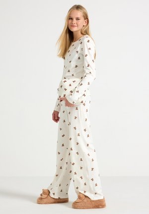 Witte pyjama set met teddybeerprint, lange mouwen en losse broek, gecombineerd met fuzzy beige slippers. Zacht, comfortabel materiaal met een ontspannen pasvorm.