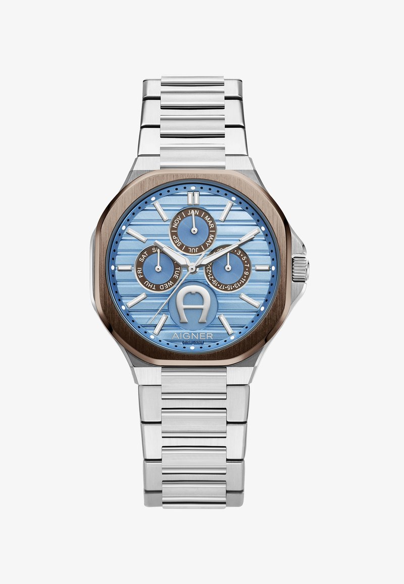 Sudraba nerūsējošā tērauda pulkstenis ar zilu teksturētu ciparnīcu, brūniem akcentiem, trim apakšciparnīcām un saites aproci. Iezīmējas ar izteiktu logotipu.