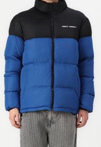 Doudoune bleu et noire avec fermeture éclair, dotée d'un col montant, de coutures horizontales et du logo "NIGHT ADDICT" sur la poitrine.