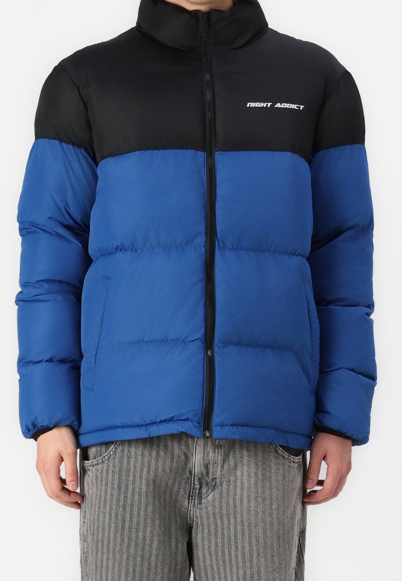 Doudoune bleu et noire avec fermeture éclair, dotée d'un col montant, de coutures horizontales et du logo "NIGHT ADDICT" sur la poitrine.