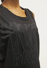 Czarny sportowy top bez rękawów wykonany z oddychającej siateczki. Posiada okrągły dekolt oraz duży, teksturowany czarny nadruk "IVY PARK".