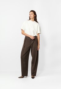 Biała bluzka z krótkim rękawem z haftem, w połączeniu z brązowymi, szerokimi spodniami z wysokim stanem o fakturowanej powierzchni. Czarne buty z ostrym noskiem.