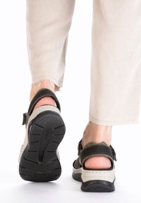 Des chaussures avec une semelle extérieure noire robuste, un dessus beige et vert olive avec des sangles réglables. Conçues pour le confort et la polyvalence.