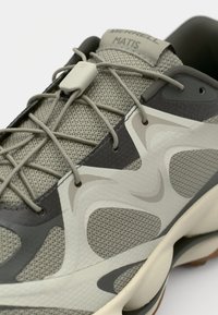 Merrell Matis shoe featuring a mesh upper in light gray, with dark gray accents and textured patterns. Flat laces and a rubber sole.
