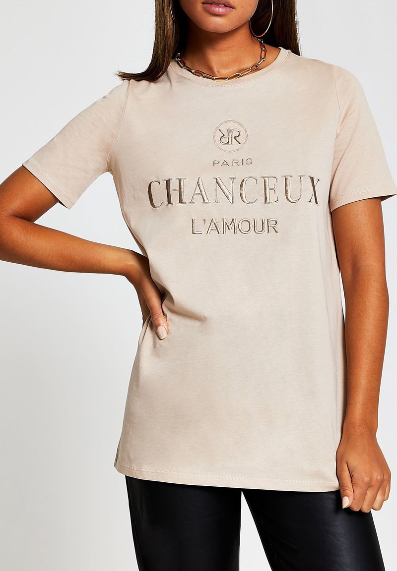 Camiseta beige de manga corta con letras en relieve "CHANCEUX L'AMOUR" y logotipo. Tejido suave, corte relajado y escote redondeado.