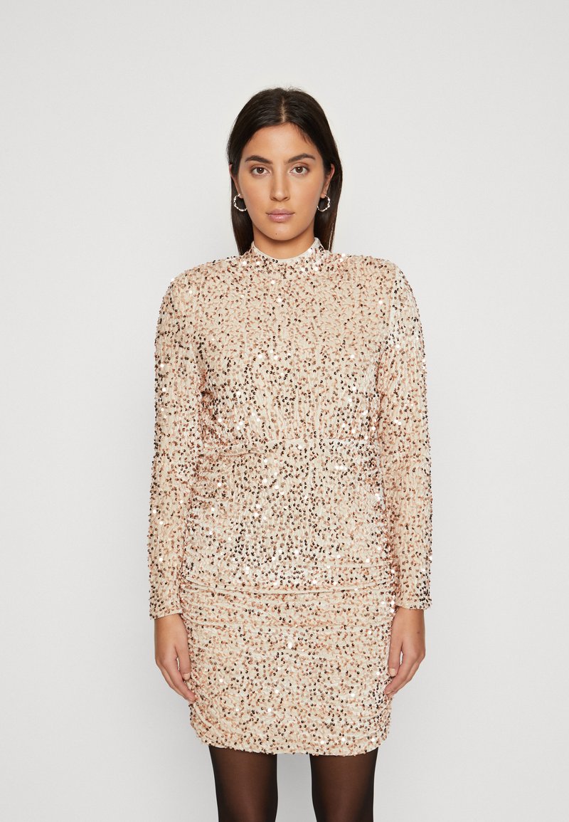 Robe mini en sequins de couleur beige doux avec des manches longues. Présente une silhouette ajustée et des détails froncés à la taille. Texture lisse avec des accents brillants.