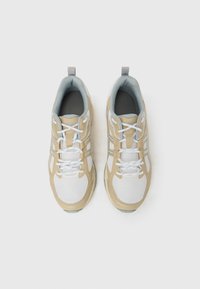 Αθλητικά παπούτσια σε μπεζ και λευκό με επάνω μέρος από δίχτυ, αντίθετες γκρίζες λεπτομέρειες και λευκά κορδόνια. Διαθέτουν επενδυμένο γιακά και υφή στη σόλα.