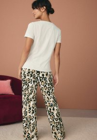 Hellgraues Kurzarm-Oberteil, kombiniert mit weit geschnittenen Hosen mit einem Leopardenmuster in Beige, Schwarz und Grün. Weicher Stoff mit glatter Textur.