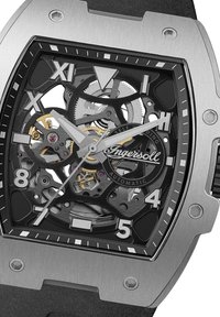 Skeleton automatisch horloge met een rechthoekige kast van roestvrij staal, zwarte wijzerplaat, zilveren wijzers en zichtbare tandwielen. Bevat gedurfde uremarkeringen.