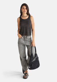 Schwarzes ärmelloses Oberteil, graue hochtaillierte weite Jeans, schwarze geflochtene Handtasche und schwarze Sandalen mit Schnallen-Detail.