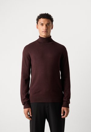 Suéter de cuello alto burdeos en una tela suave, diseño ajustado, mangas largas y puños acanalados, combinado con pantalones negros.