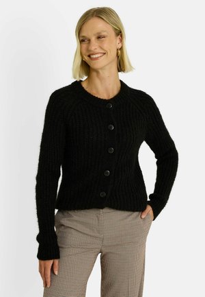 Cardigan en tricot noir avec une texture côtes, encolure ronde et cinq boutons noirs, porté sur un pantalon à carreaux.