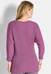 Lila gerippter Strickpullover mit Rundhalsausschnitt, dreiviertellangen Ärmeln und geradem Saum. Der Stoff hat eine strukturierte Oberflächenbeschaffenheit.