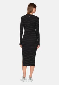 Black knitted dress with a fitted silhouette, featuring a subtle zebra pattern and long sleeves. Back design includes a round neckline and slit.