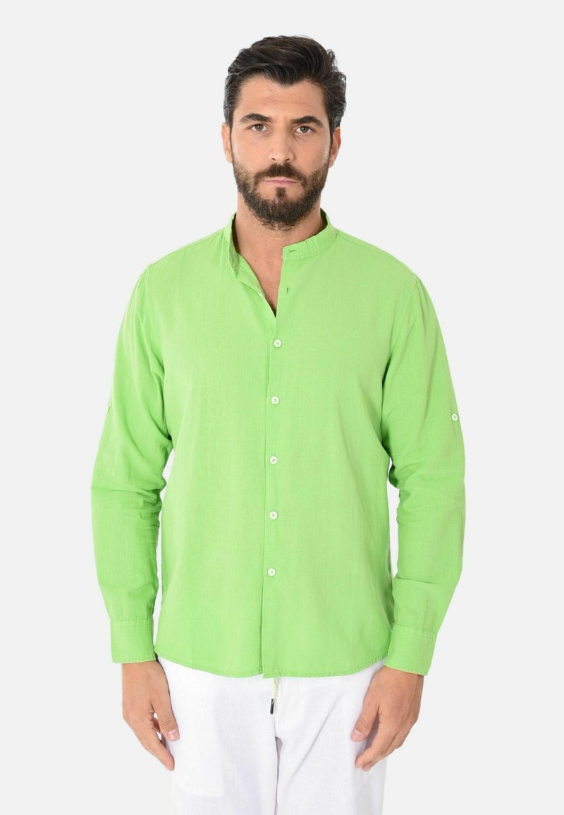 Camicia verde a maniche lunghe con colletto a bandiera, chiusura frontale con bottoni e texture visibile. Indossata con pantaloni bianchi, presenta un orlo dritto e polsini.