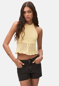 Cropped top giallo lavorato a maglia con un corpo testurizzato e un motivo traforato vicino all'orlo, abbinato a pantaloncini di jeans neri.