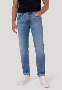 Jeans en denim bleu clair avec une coupe droite, dotés de poches classiques, d'un léger délavage et de ourlets roulés, associés à des baskets blanches.