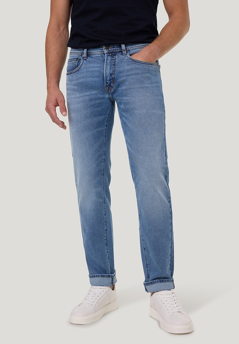 Jeans en denim bleu clair avec une coupe droite, dotés de poches classiques, d'un léger délavage et de ourlets roulés, associés à des baskets blanches.