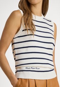 Fehér ujjatlan kötött felső sötétkék vízszintes csíkokkal, bordázott nyakkivágással és szegéllyel, deréknál hímzett logóval.
