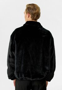Zwarte fleece jack met een hoge kraag, losvallend ontwerp en textuur oppervlak. Bevat elastische manchetten en zoom voor een strakke pasvorm.