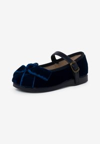 Zapato de terciopelo azul marino con punta redonda, un lazo decorativo en la parte delantera y una correa con hebilla negra para un ajuste seguro. Suela plana de goma.