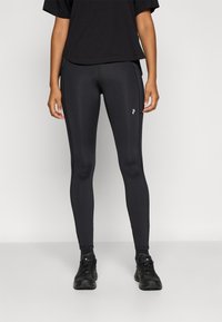 Czarne legginsy sportowe o dopasowanym kroju z delikatnym połyskiem, zestawione z luźną czarną bluzą. Buty są czarne, z sznurowadłami i fakturowanym wzorem.