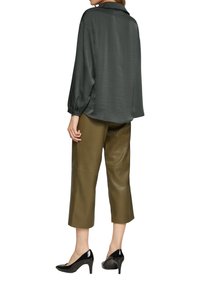 Donkergroene satijnen blouse met een losse pasvorm en lange mouwen, gecombineerd met olijfgroene cropped leren broek en zwarte gepatineerde leren hakken.